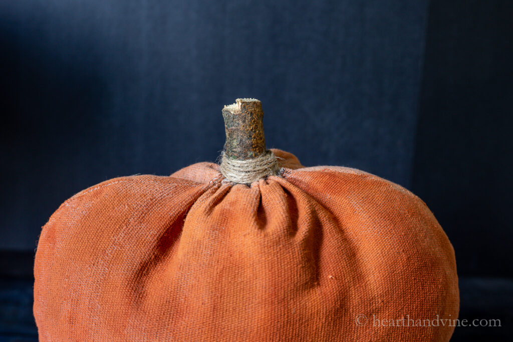 Top of fabric pumpkin with tree branch stem and twine.