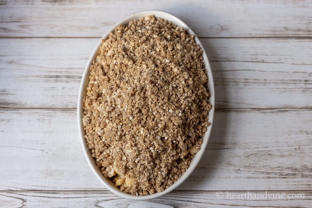Apple crisp with oats in an oval baking dish before cooking.