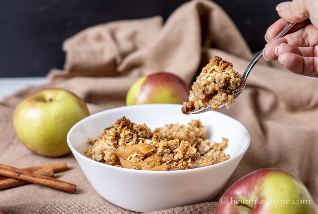 Bowl of apple crisp with oat and a spoon with a bite lifted out of bowl.