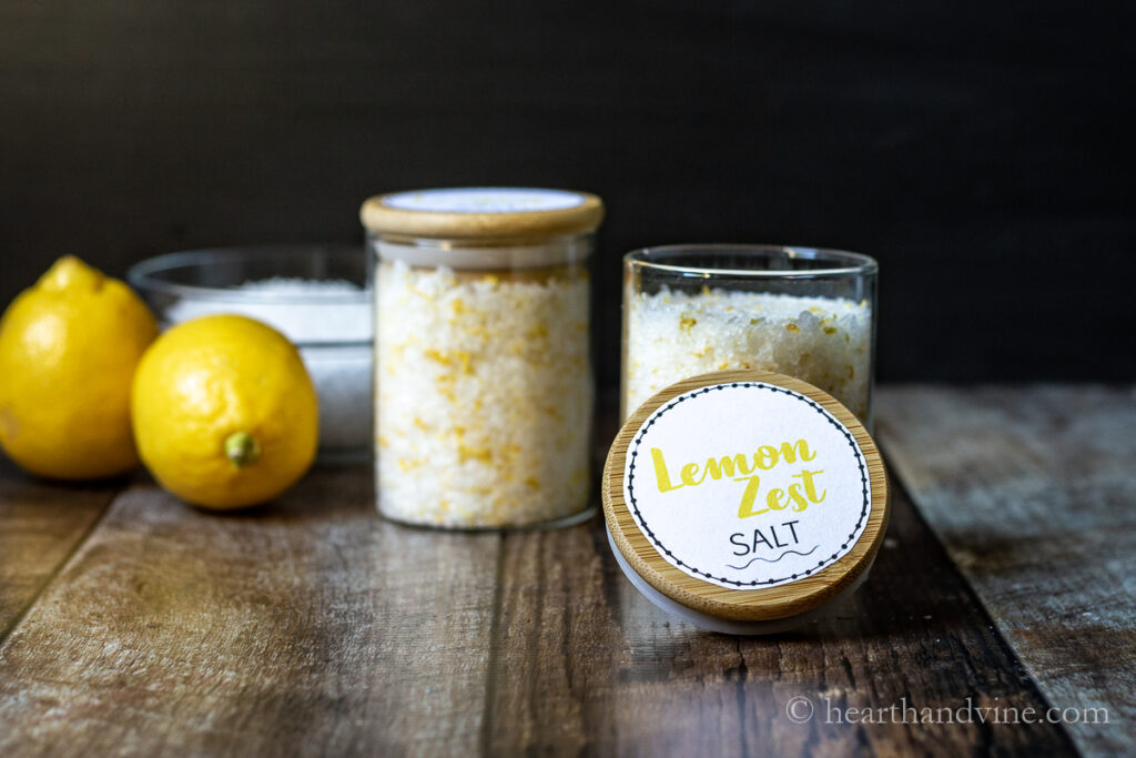 Lemons, bowl of salt and glass jars with lemon zest salt with labels on top.