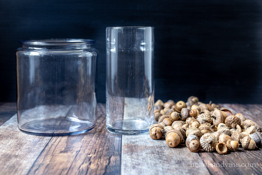 An apothecary jar, a tall vase and several acorns.