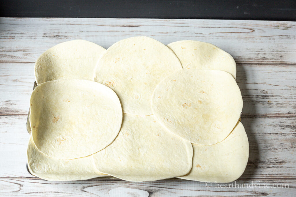 Flour tortillas laid out all over a sheet pan with the edges hanging off the sides.