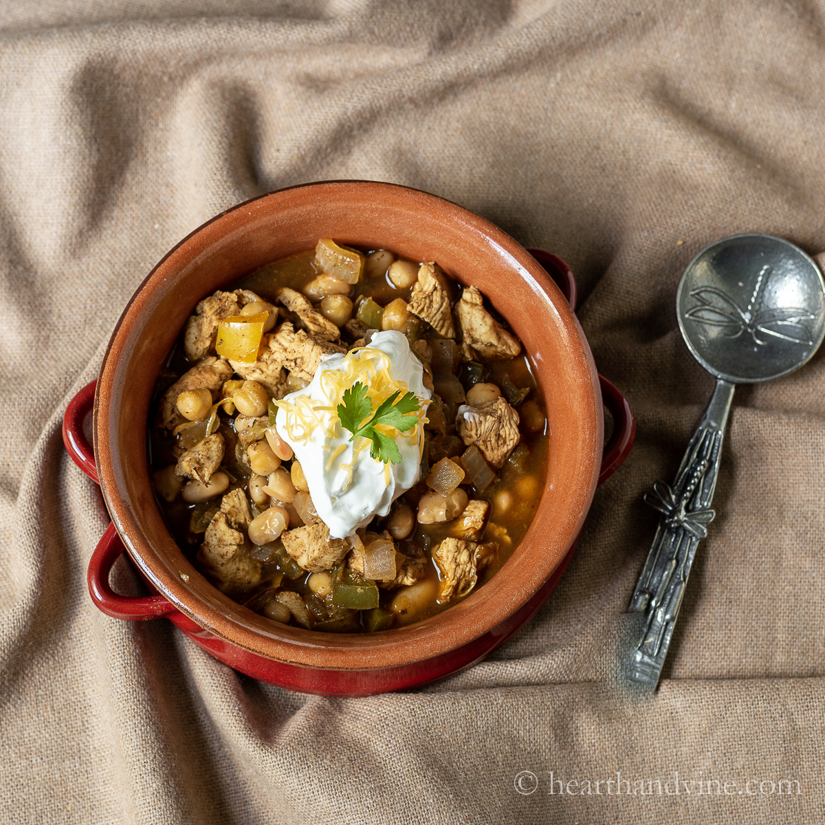 Bowl of spicy chicken chili with a dollop of sour cream, some shredded cheese and a cilantro leaf on top.