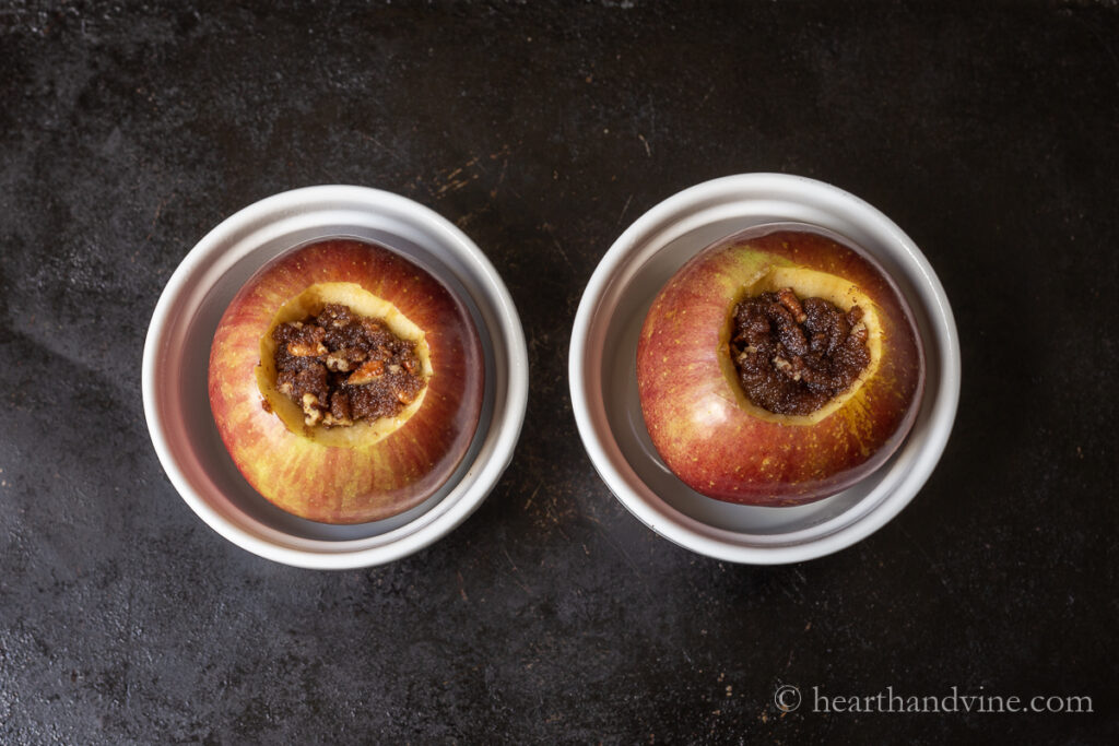 Two apples in ramekins with sugar, cinnamon and pecan stuffing.