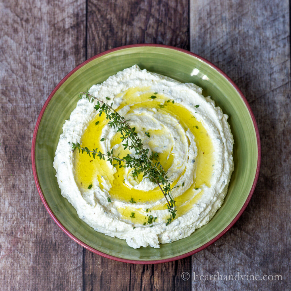 Bowl of whipped feta dip with olive oil drizzle and fresh thyme sprigs.