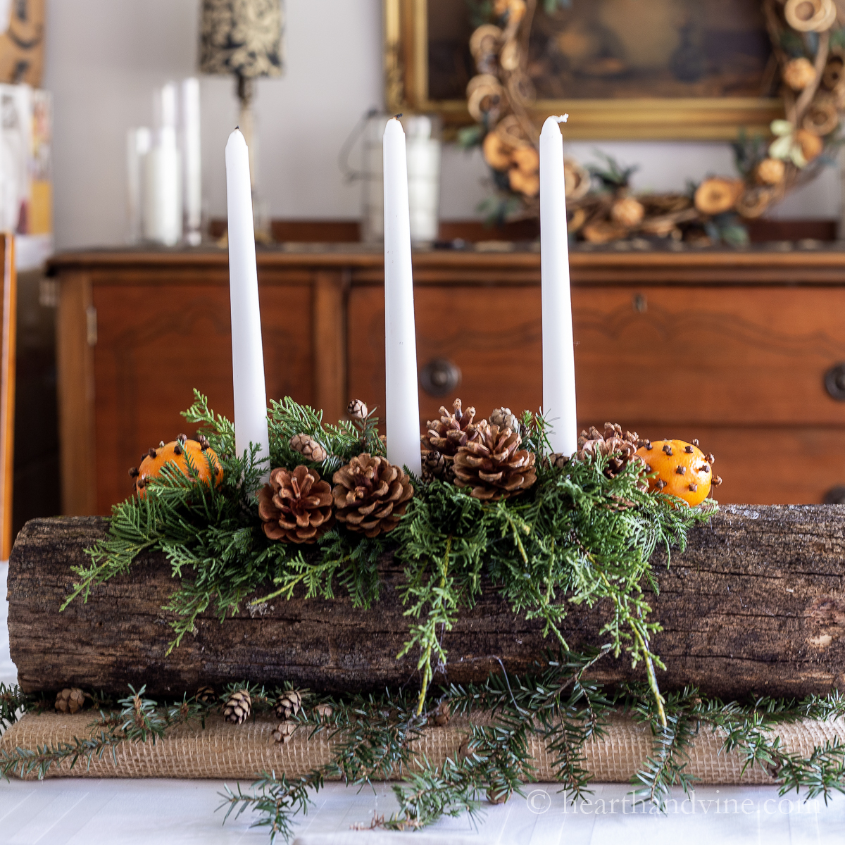 Yule log decorated with evergreens, three white candles, pine cones and pomanders.