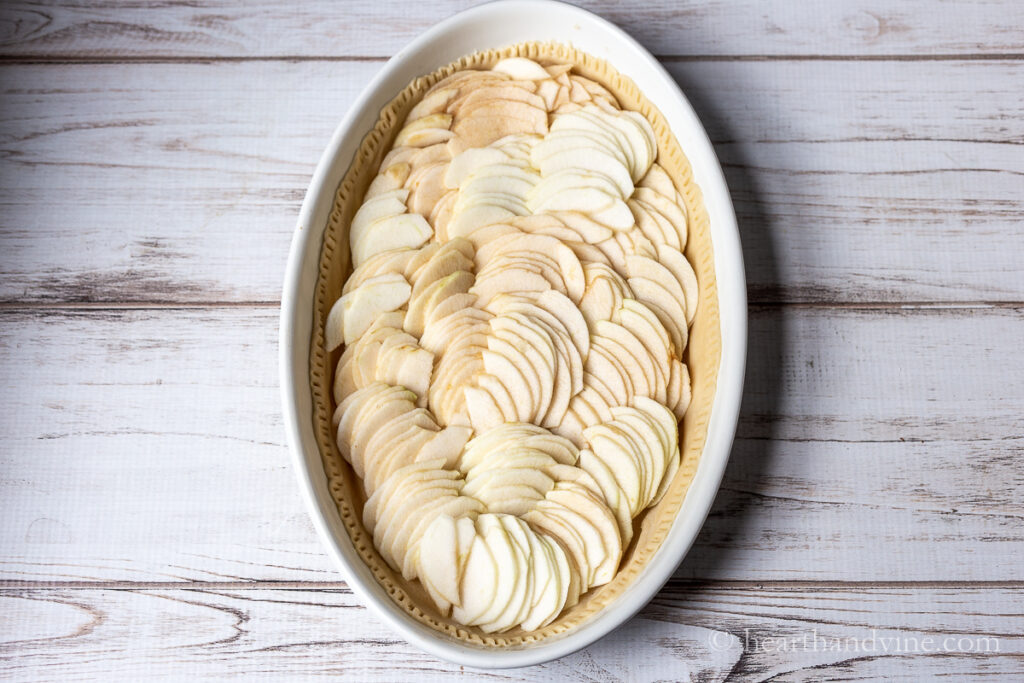 Thinly sliced apples all over a pie crust in an oval baking dish.