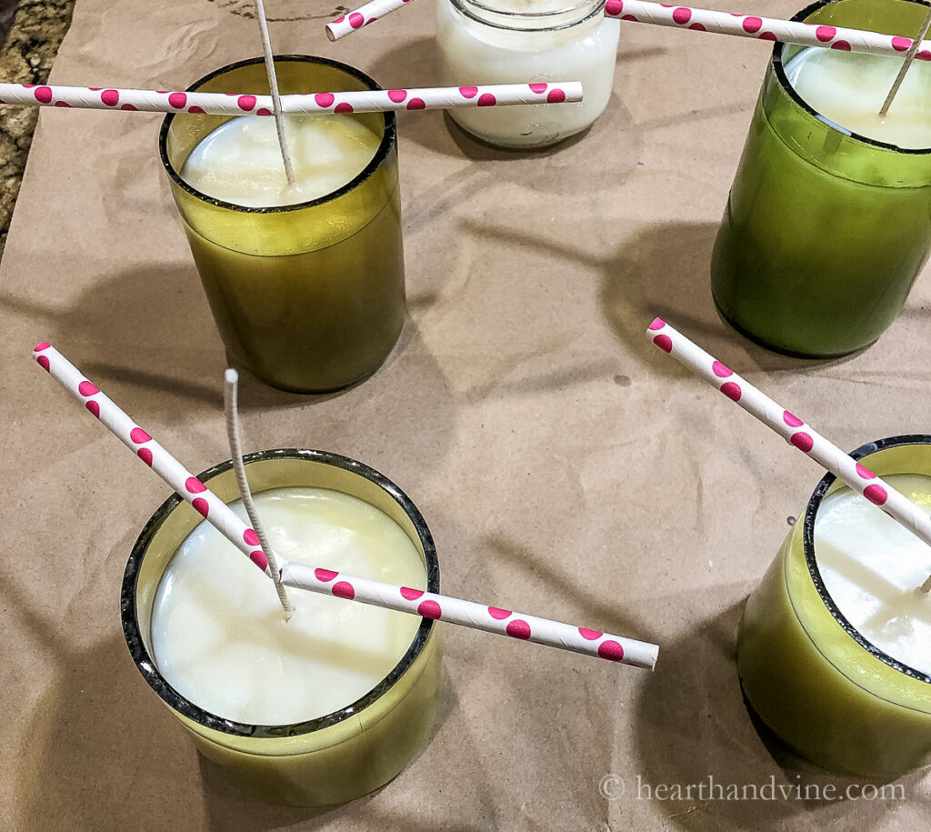 Wine bottle candle wax becoming opaque with wicks being held with paper straws.