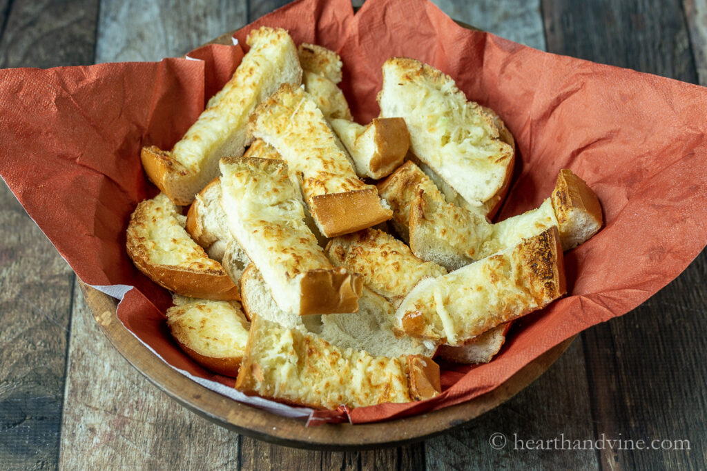 Napkin lined basket filled with slices of cheesy garlic bread.