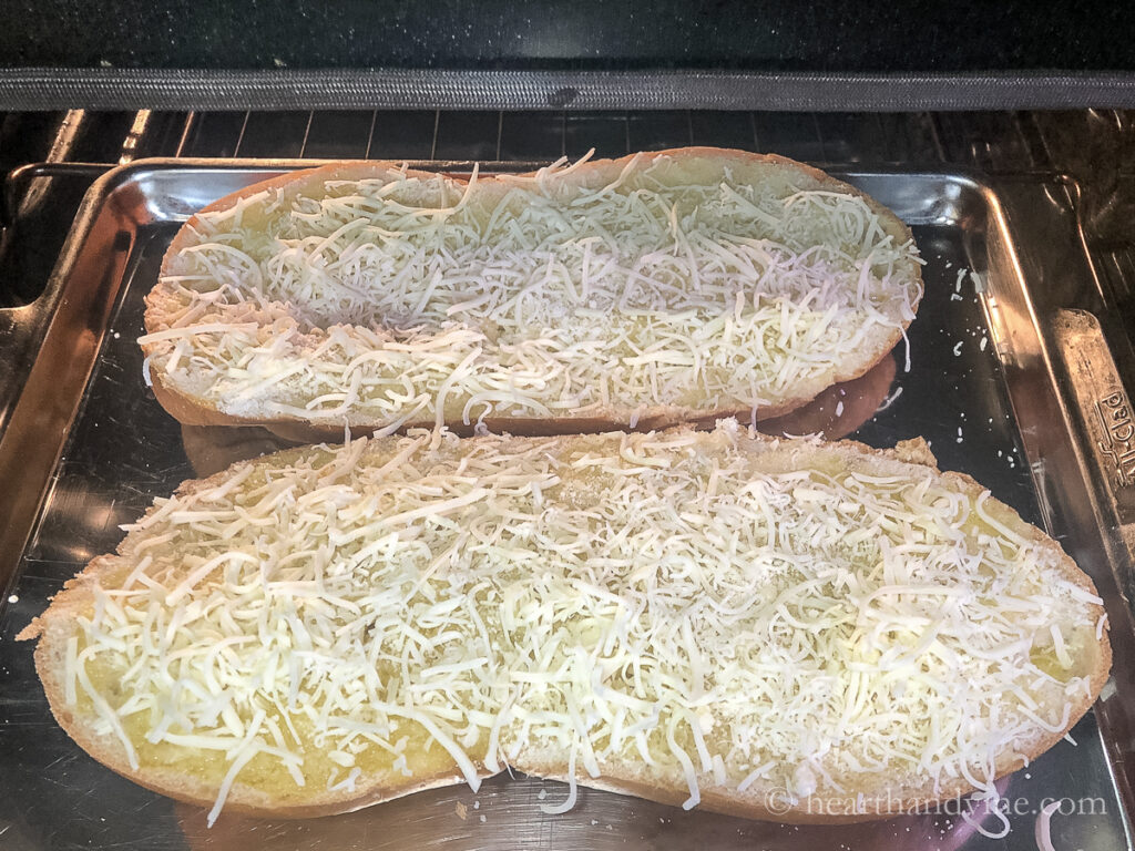 Large Italian bread loaf sliced in half with garlic butter and cheese set in the oven to cook.