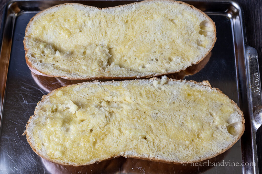 Italian bread sliced lengthwise, placed on a baking sheet and slathered with garlic butter.