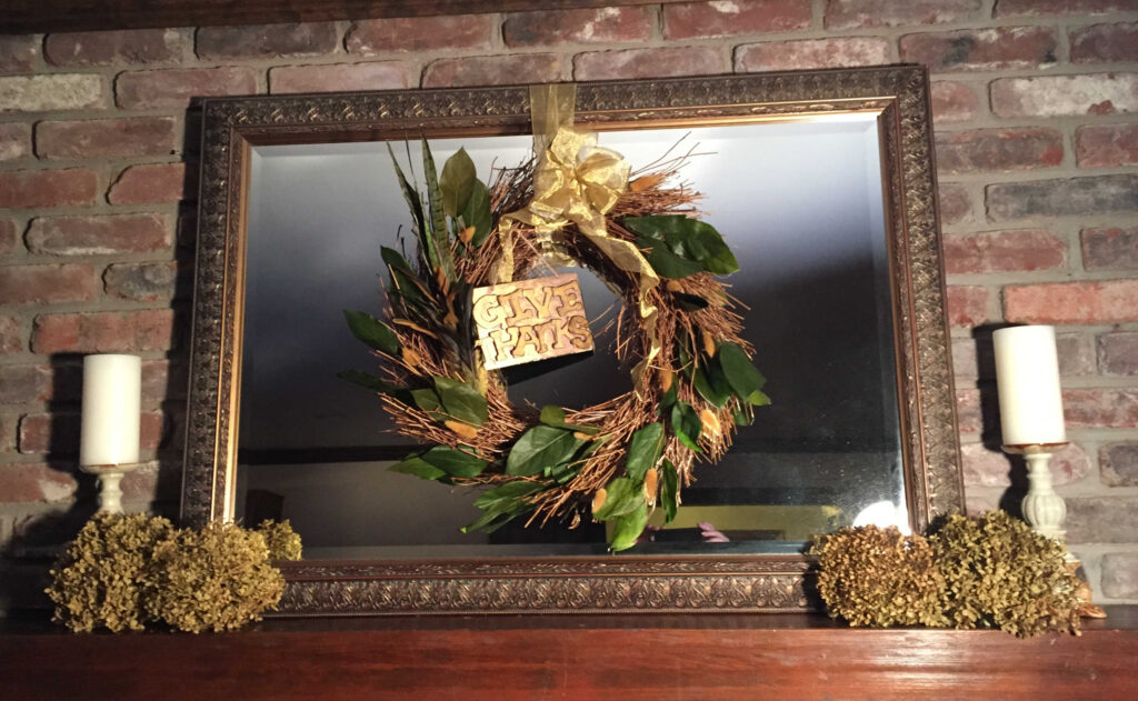 Give thanks wreath on a mirror on a mantel with dried hydrangeas and candles on the sides.