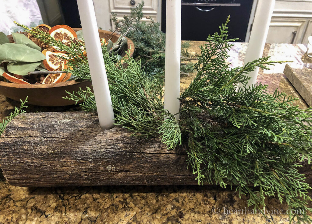 A yule log with three white candles and some evergreens.