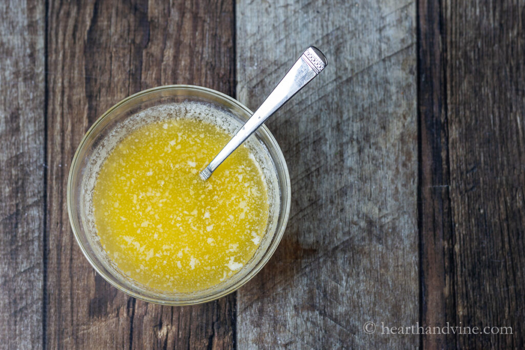 Small bowl with a spoon containing melted butter and grated garlic.