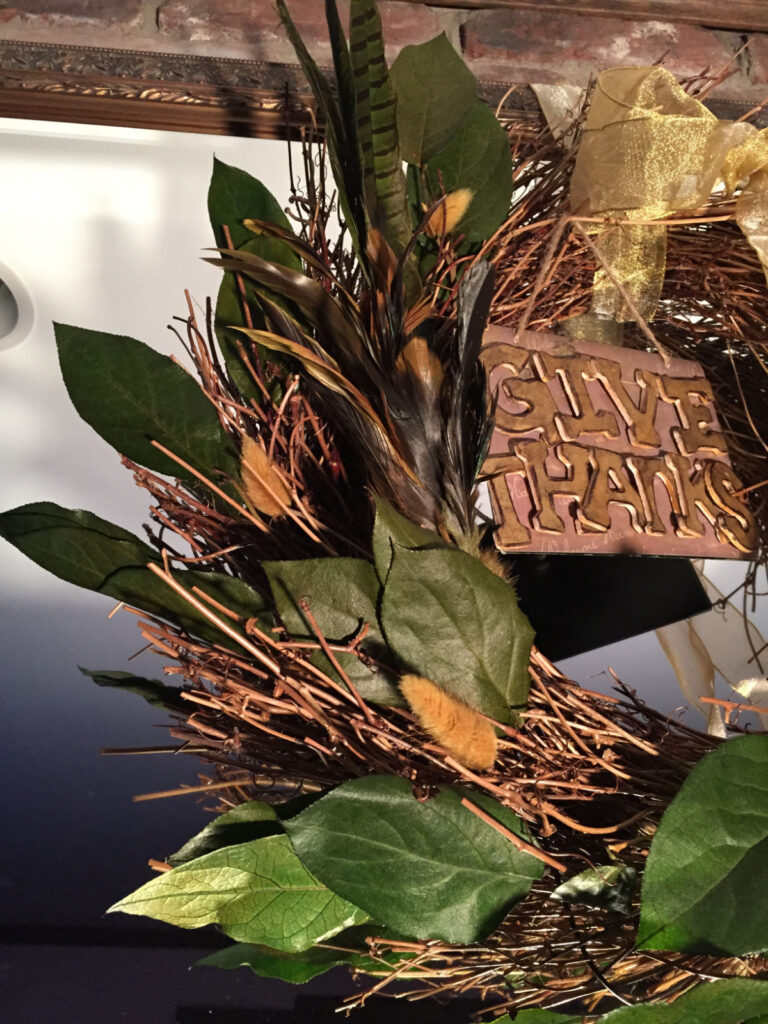 Thanksgiving wreath with sisal leaves, feathers, a gold bow and a Give Thanks sign.