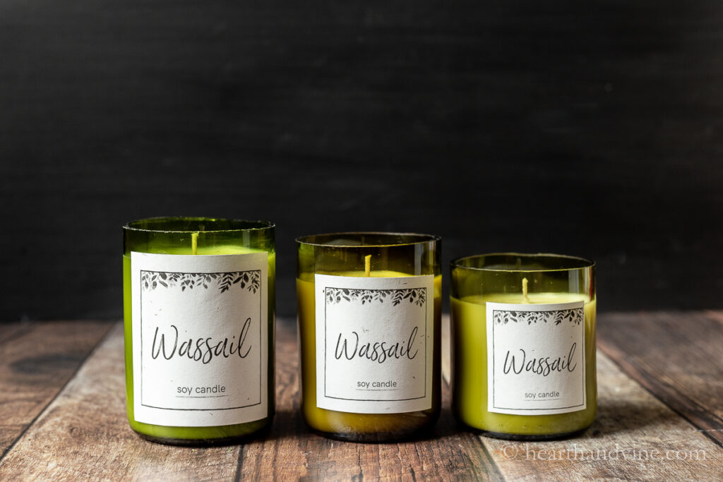 Trio of wine bottle candles with labels that say "Wassail" and soy candle.