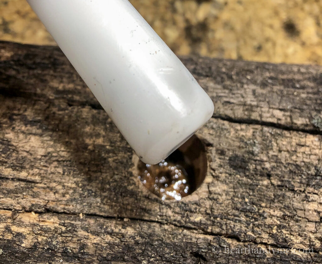 Melted wax in a hole in a log with a taper candle ready to set into the hole.