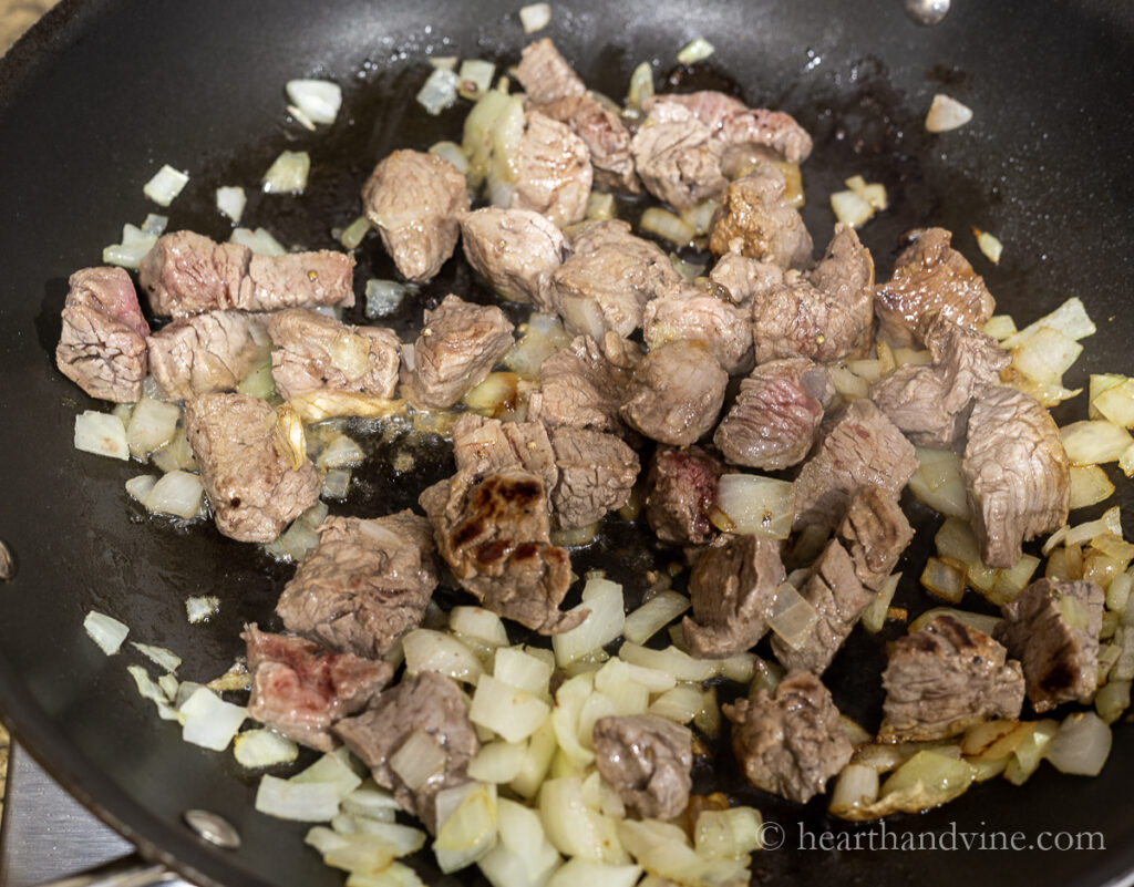 Cubes of beef stewing meat sautéed with onions in a pan.