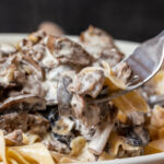 A fork lifting a bit of noodles, beef and mushrooms in a creamy sauce.