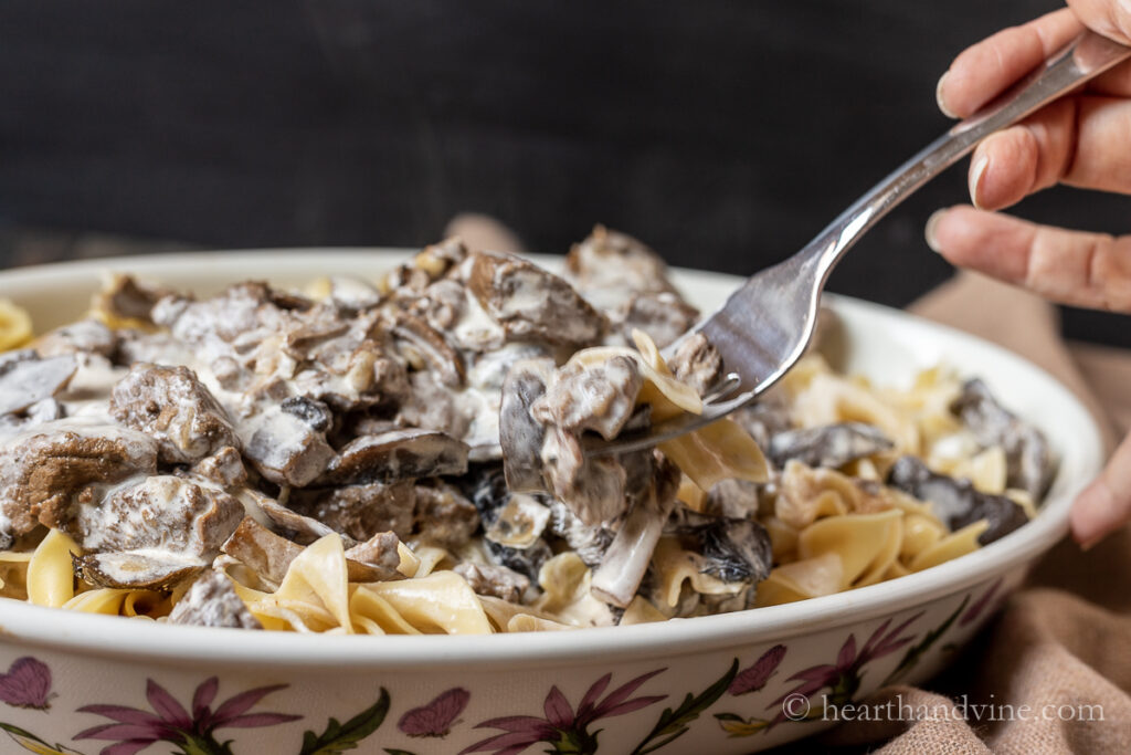 A fork lifting a bit of homemade beef stroganoff with noodles, mushrooms and a creamy sauce.