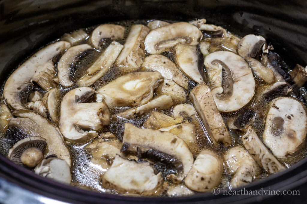 Slice baby portabella mushrooms floating in broth in a slow cooker.