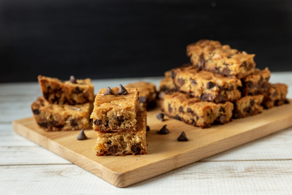 Salted caramel blondies stacked up on a wooden tray with chocolate chips scattered around.