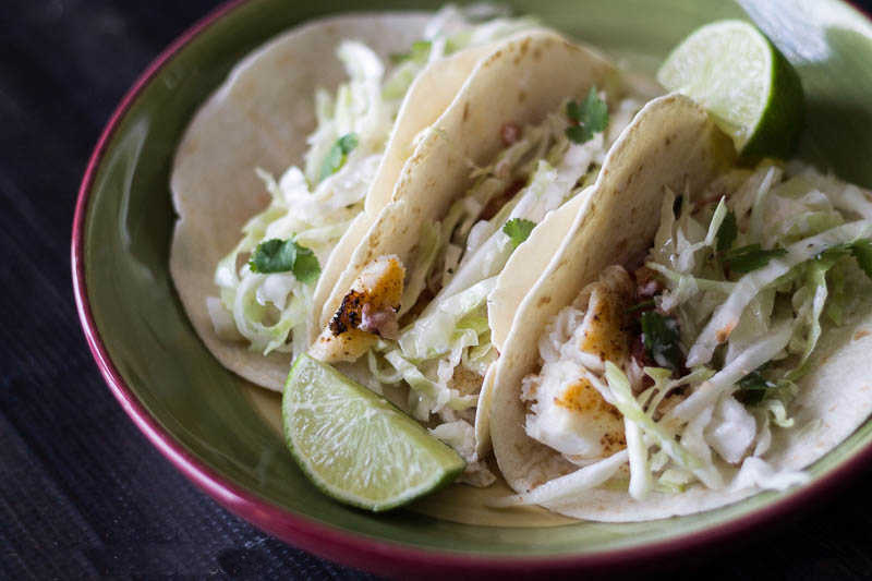 Three fish tacos with slaw in a bowl with a lime wedge.