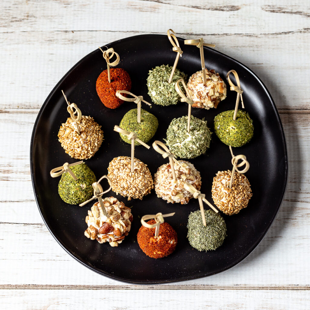 Mini cheese balls coated in nuts, spices and seeds on a black dish.