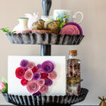Two tiered tray decorated for Valentine's Day with paper flowers, candles and other trinkets