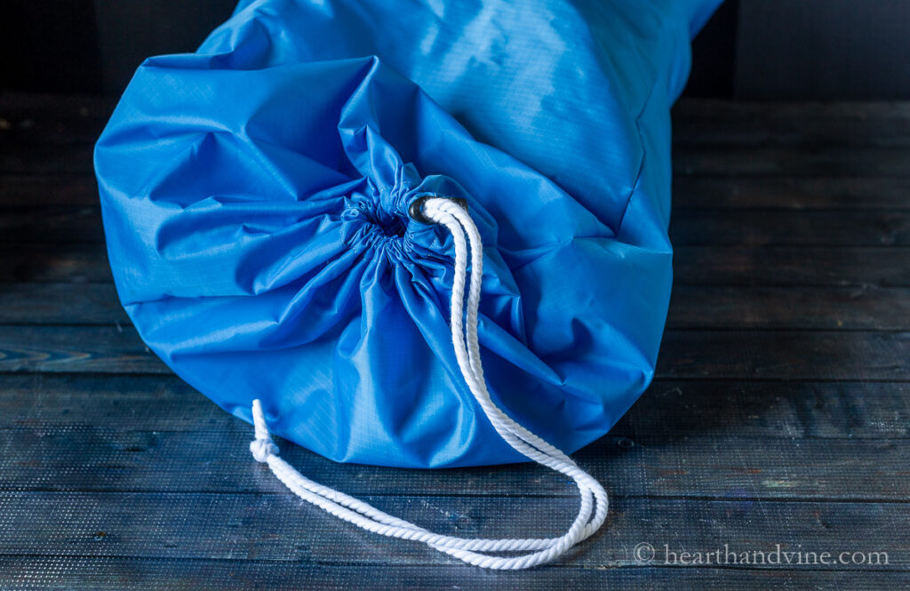 Nylon blue travel laundry bag with clothes inside gathered at the top.
