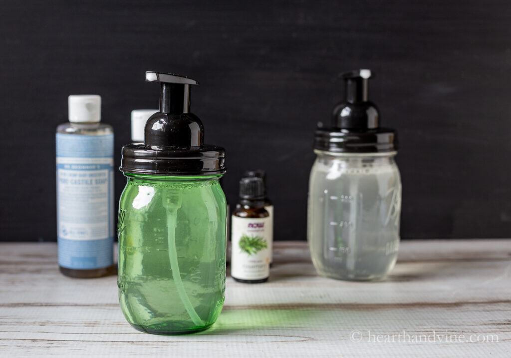 Green pint sized mason jar foaming soap dispenser in front of a clear jar, essential oils and castile soap.