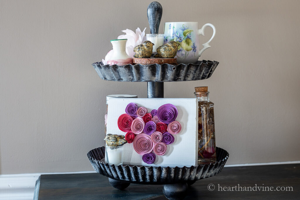 Two tiered tray with ceramic birds, wood block with a paper flower heart, pink and white vase,, floral cup and herbarium bottle.