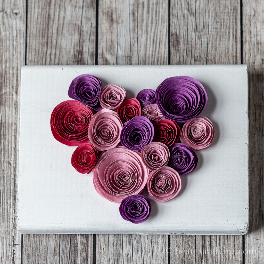 Rolled paper flowers glued onto a white wooden block in the shape of a heart.
