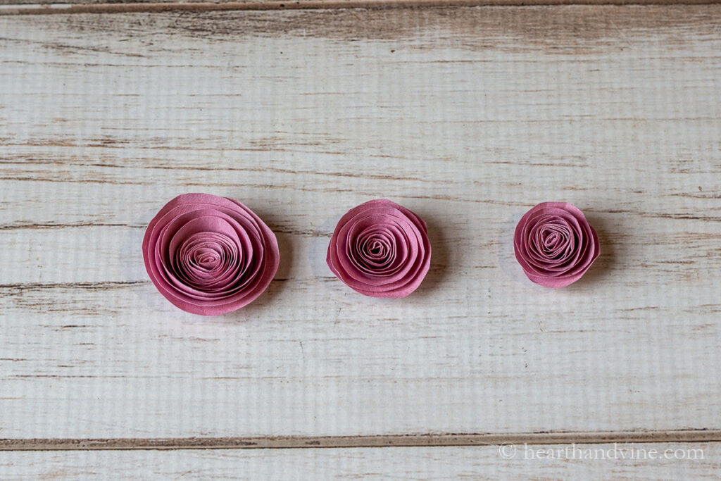 Three different sized rolled paper flowers in pink.