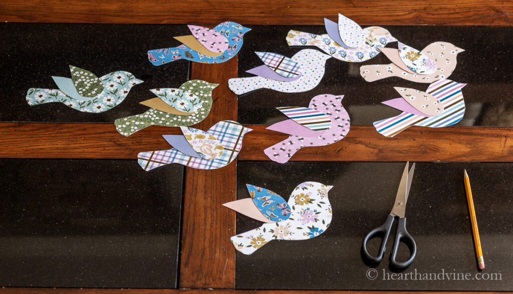 9 paper birds in different prints on a table with scissors and a pencil.