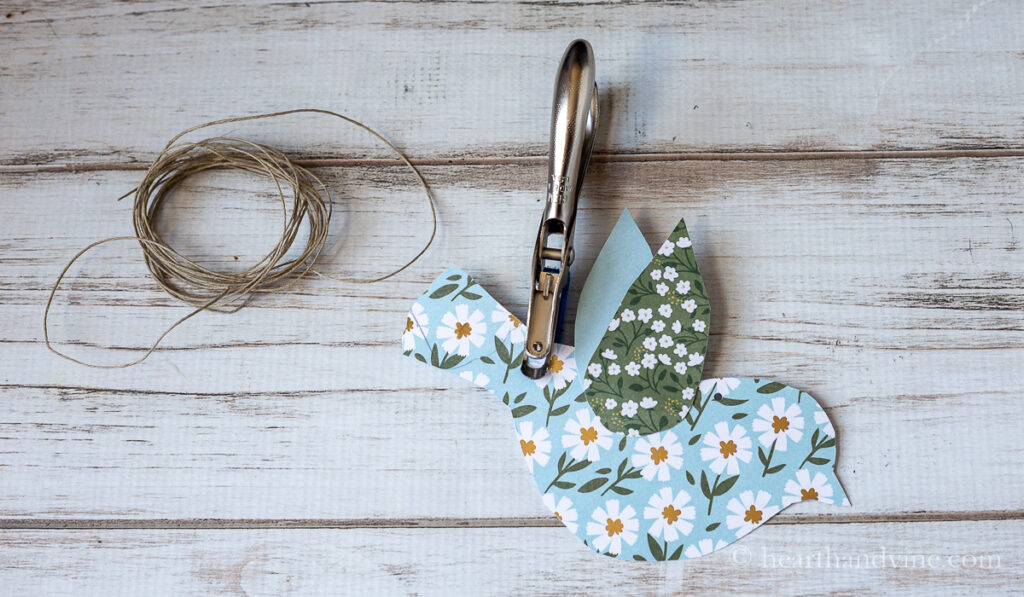 Blue flowered paper bird with a mini paper punch on the back of the bird next to a section of twine.