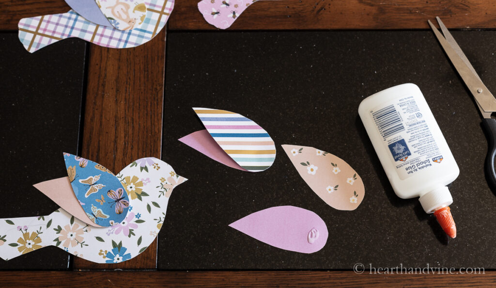 Bird wings in different paper prints with white glue and one bird with wings attached.