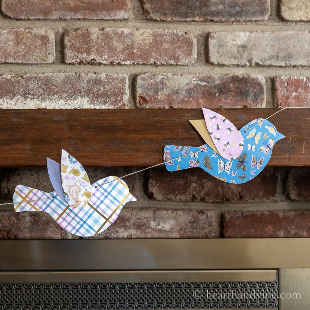 Paper bird garland on jute hanging on fireplace mantel.