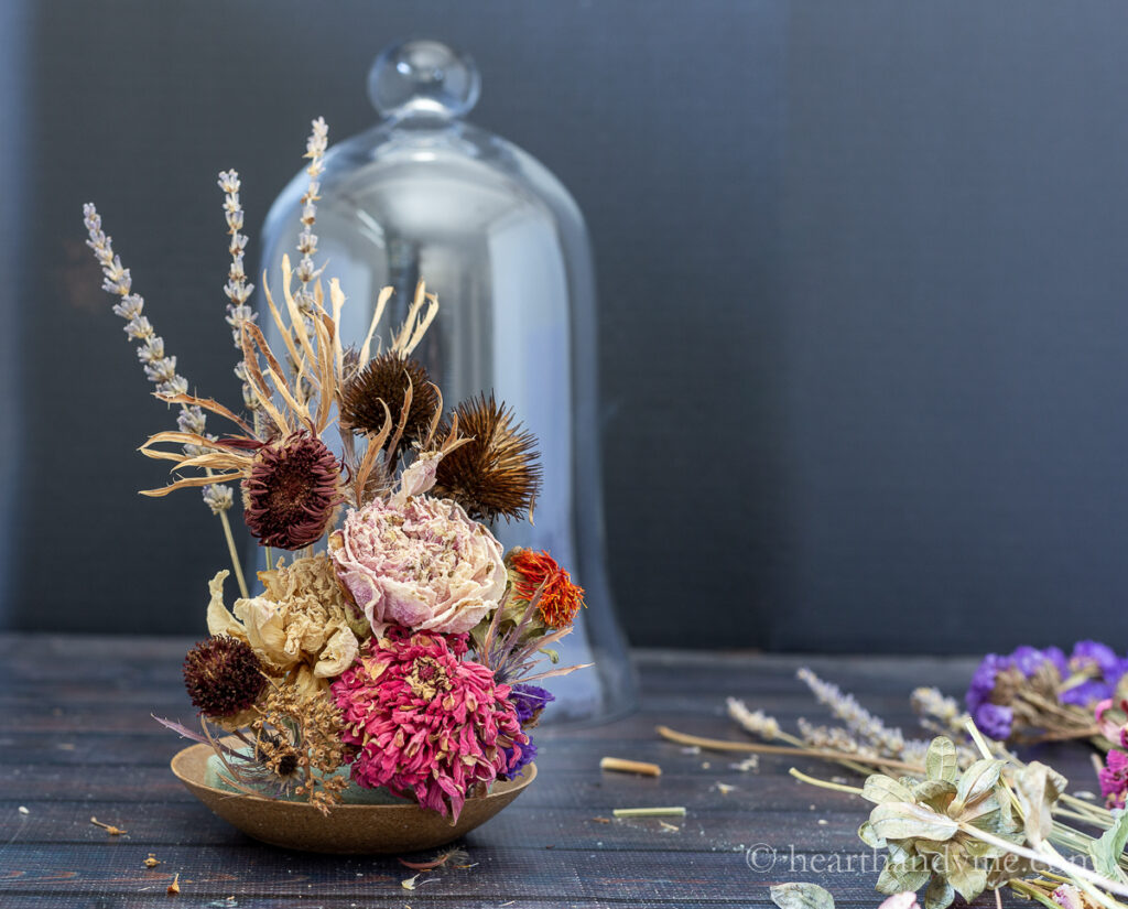 Dried peonies, zinnia and other flowers arranged in floral foam on a plant pot saucer.