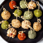 Collection of mini cheese balls with bamboo skewers on a black plate.