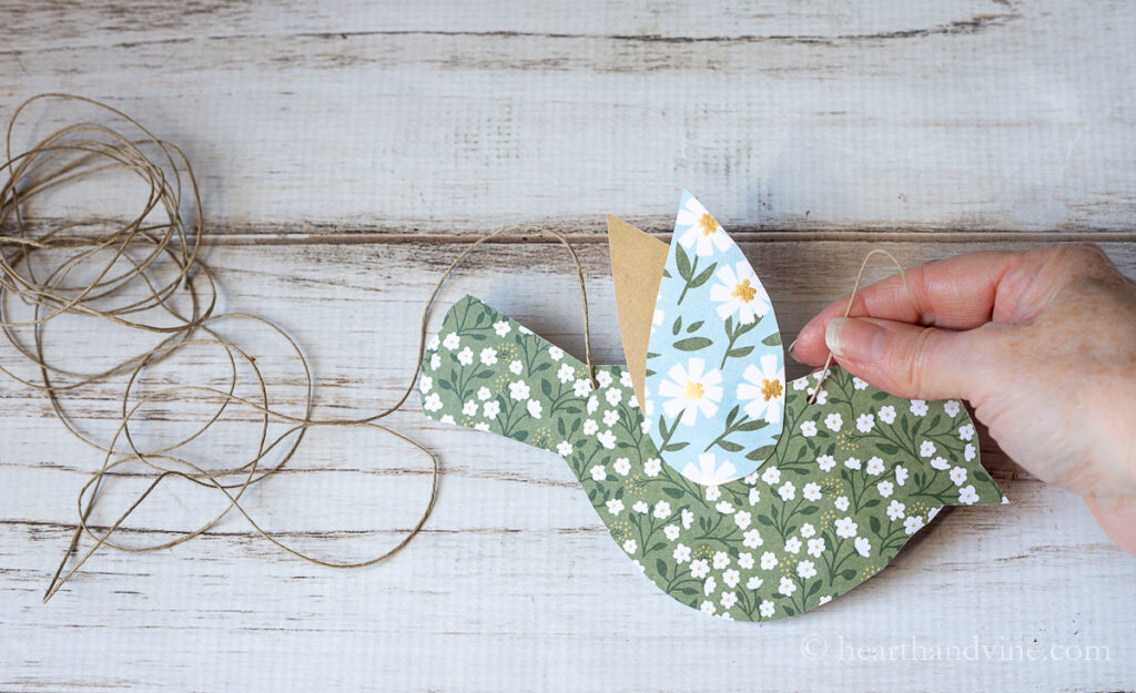 Twine garland threading through a paper bird with two holes punched out.