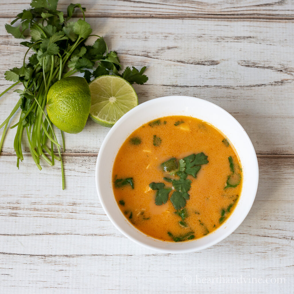 Red chicken curry soup with coconut milk in a bowl with fresh cilantro and limes.