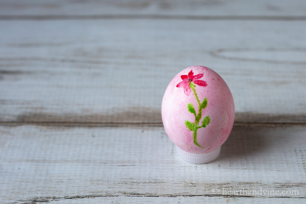 A red painted watercolor Easter egg with a red flower and stem painted on top.