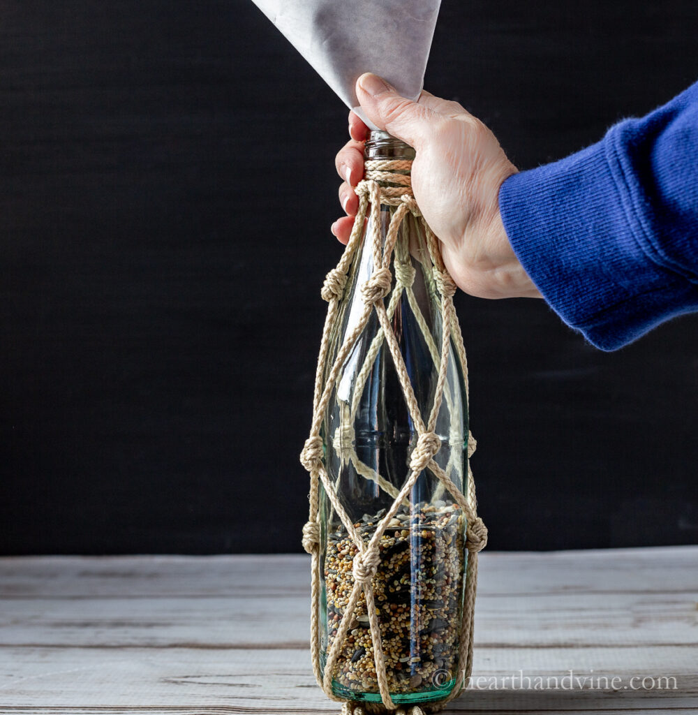 Filling a bottle with birdseed using a paper funnel.