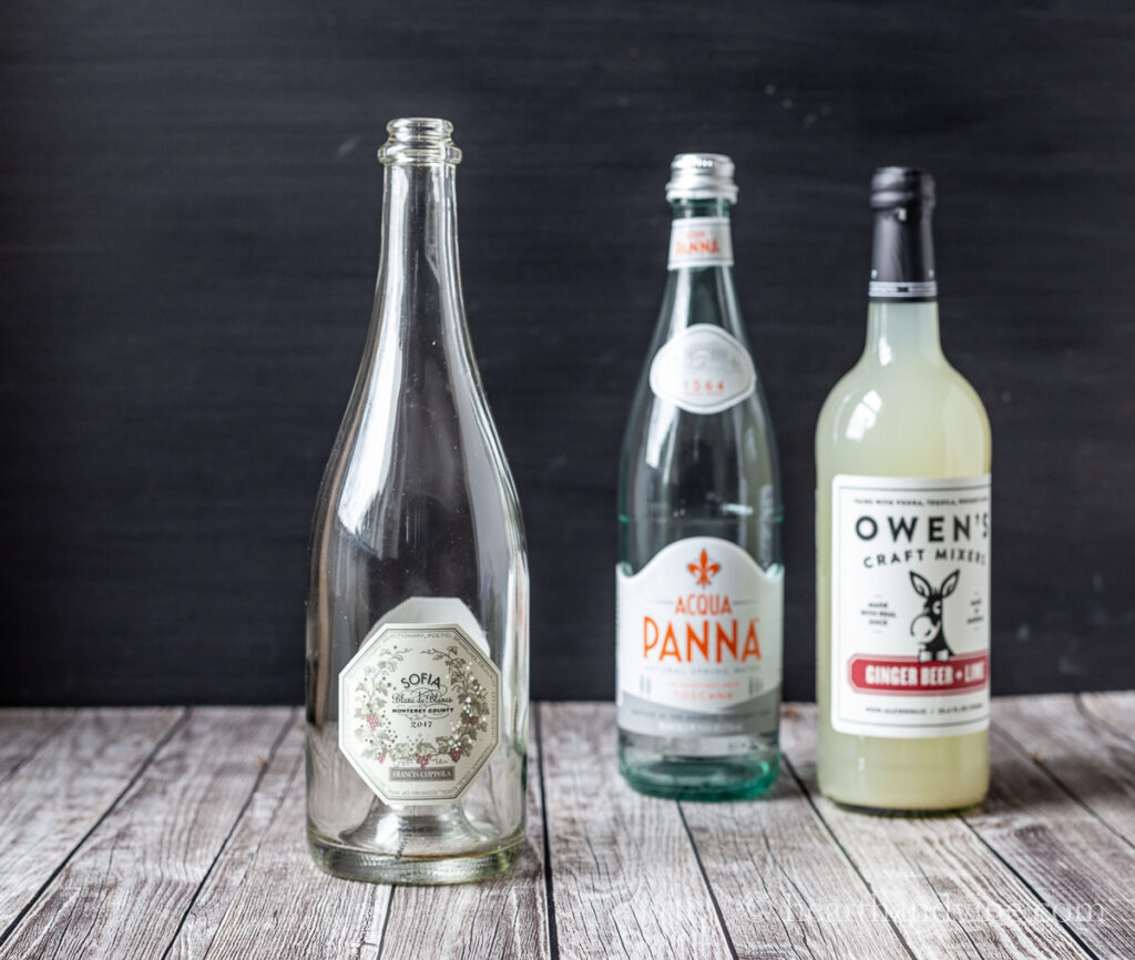Empty champagne bottle, a large glass water bottle and a large glass ginger beer mixer bottle.