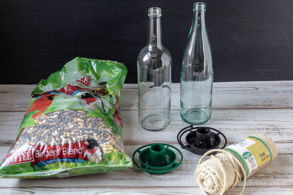 Two tall glass bottles, a bag of bird seed, macrame cording and two bird feeder bottle attachments.