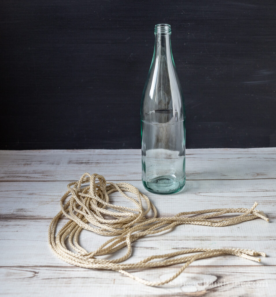 Large glass bottle next to four long lengths of nylon macrame cording.