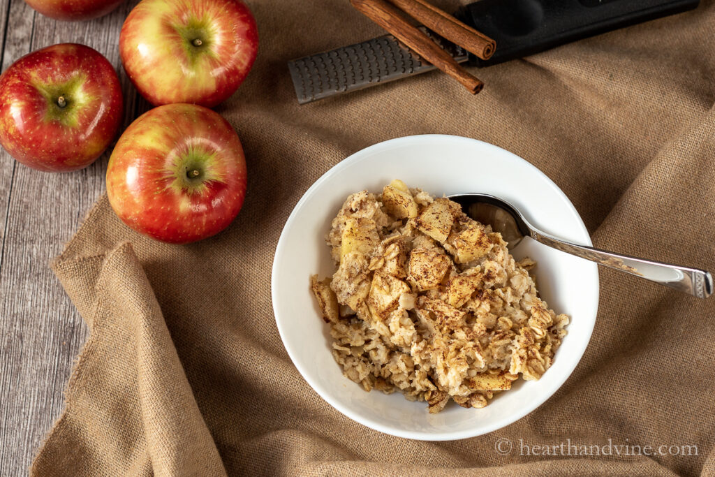 Apples, cinnamon sticks and a bowl of apple pie baked oatmeal with a spoon.