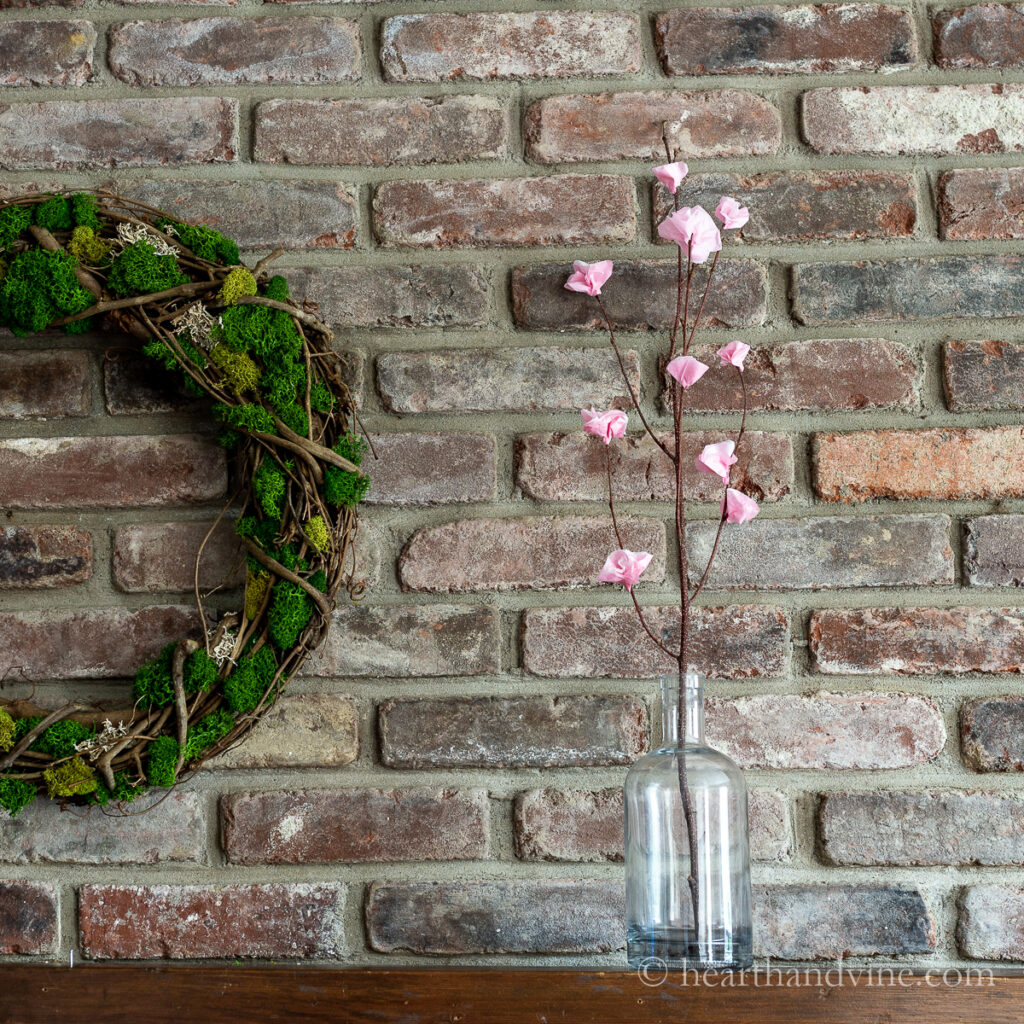 Paper cherry blossoms on a branch in a bottle vase on a mantel.