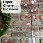 Paper cherry blossom branch in a bottle vase on a mantel.